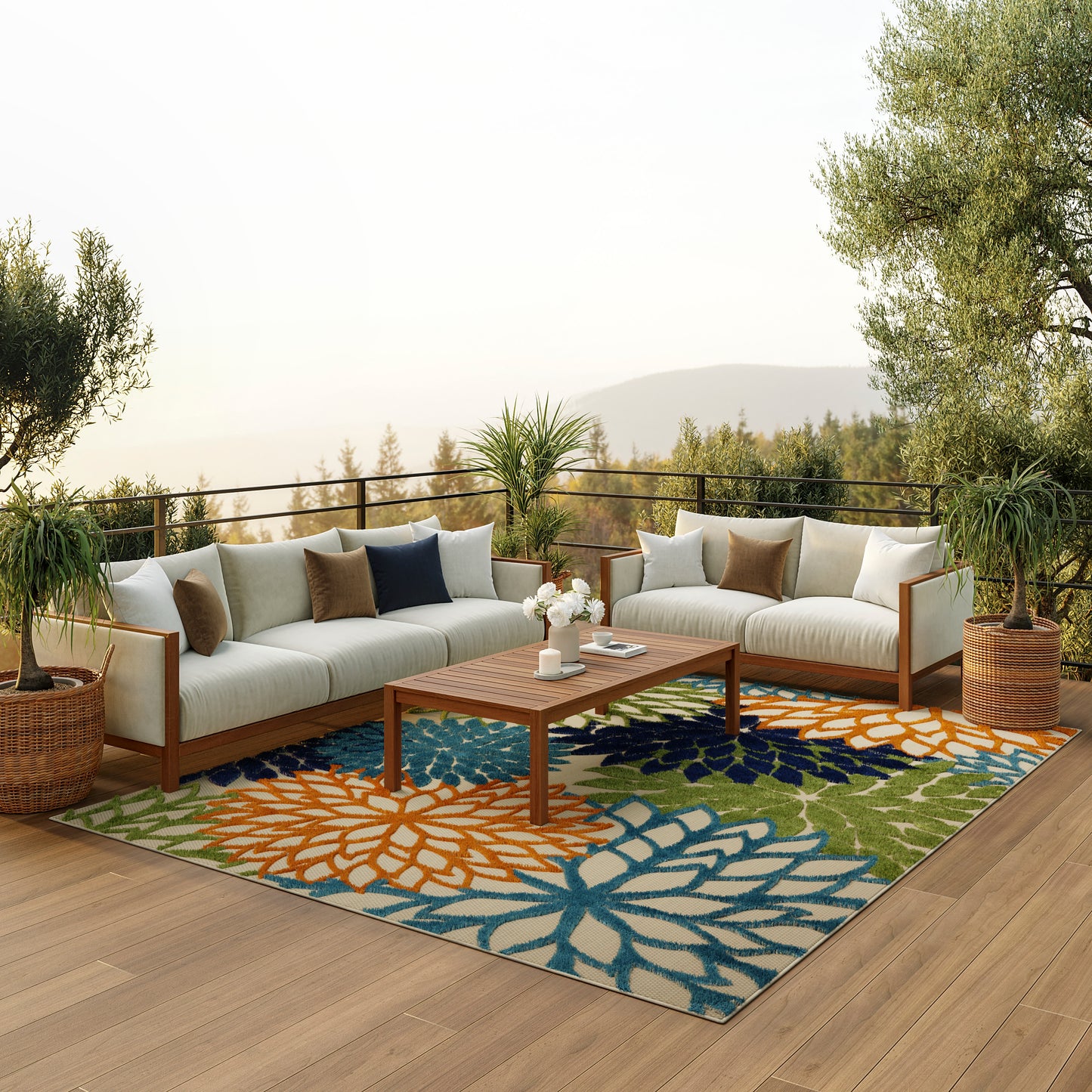 Outdoor wooden-framed sectional sofa with beige cushions on a colorful floral rug, potted plants & hillside backdrop.