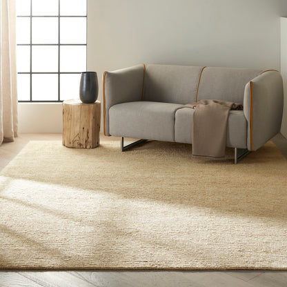 Light gray sofa with mustard piping, beige throw, sunlit living room with natural fiber rug and black vase on a stump table.