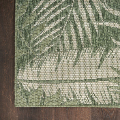Green palm-leaf patterned woven rug on wood floor; beige background with dark green border and textured weave.