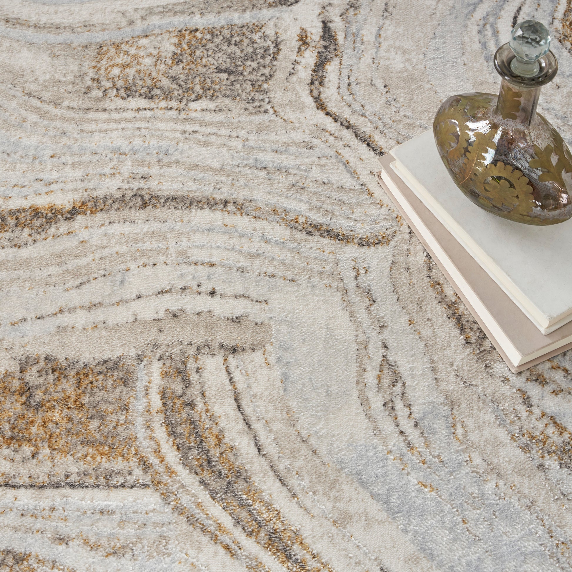 Beige, cream and gray abstract patterned rug with a vintage glass decanter atop light hardcover books.