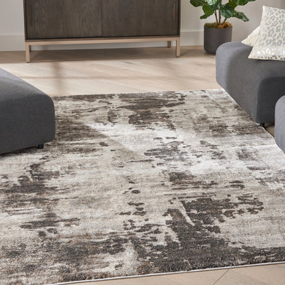 Distressed abstract gray and beige area rug on light wood floor in a modern living room.