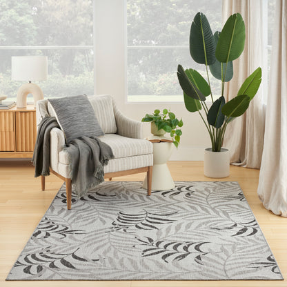Beige striped armchair with wooden legs, gray throw, palm-leaf rug, large potted tropical plant in a bright living room.