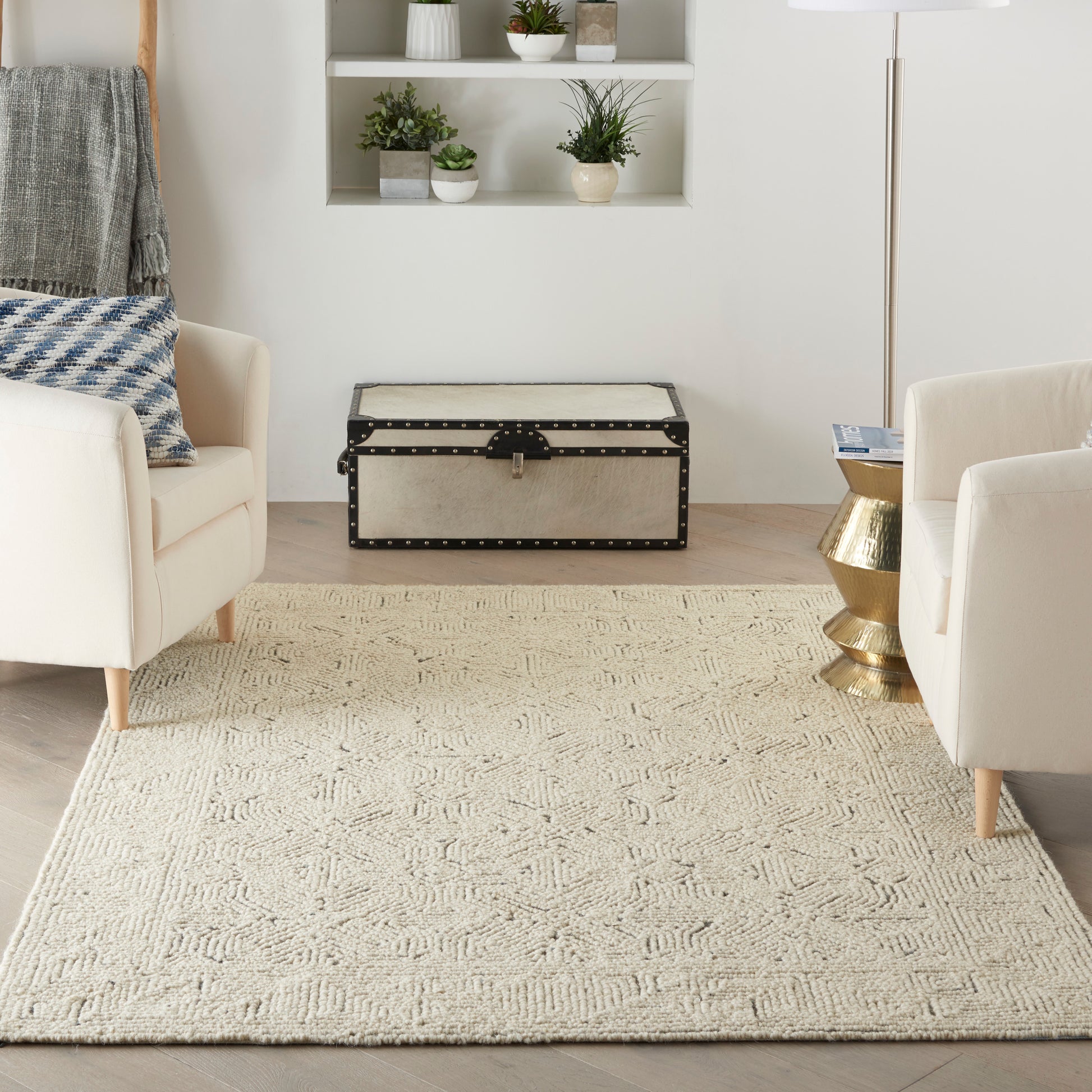 Cream textured area rug in a modern living room with beige armchairs and a vintage beige storage trunk.