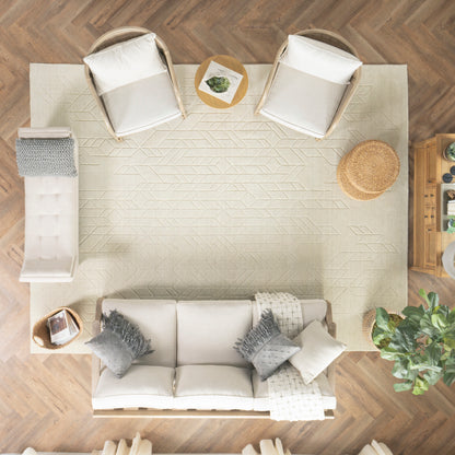 Overhead view of a neutral living room with a cream sofa, two beige chairs, a rug on a wooden floor, wicker mat, and plants
