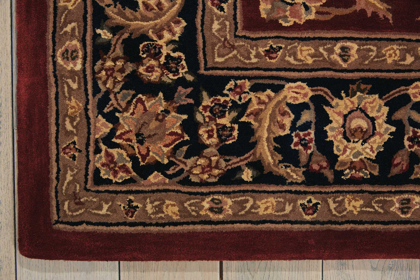 Rectangular Persian-style rug with burgundy, ivory, and gold floral border on a wooden floor.