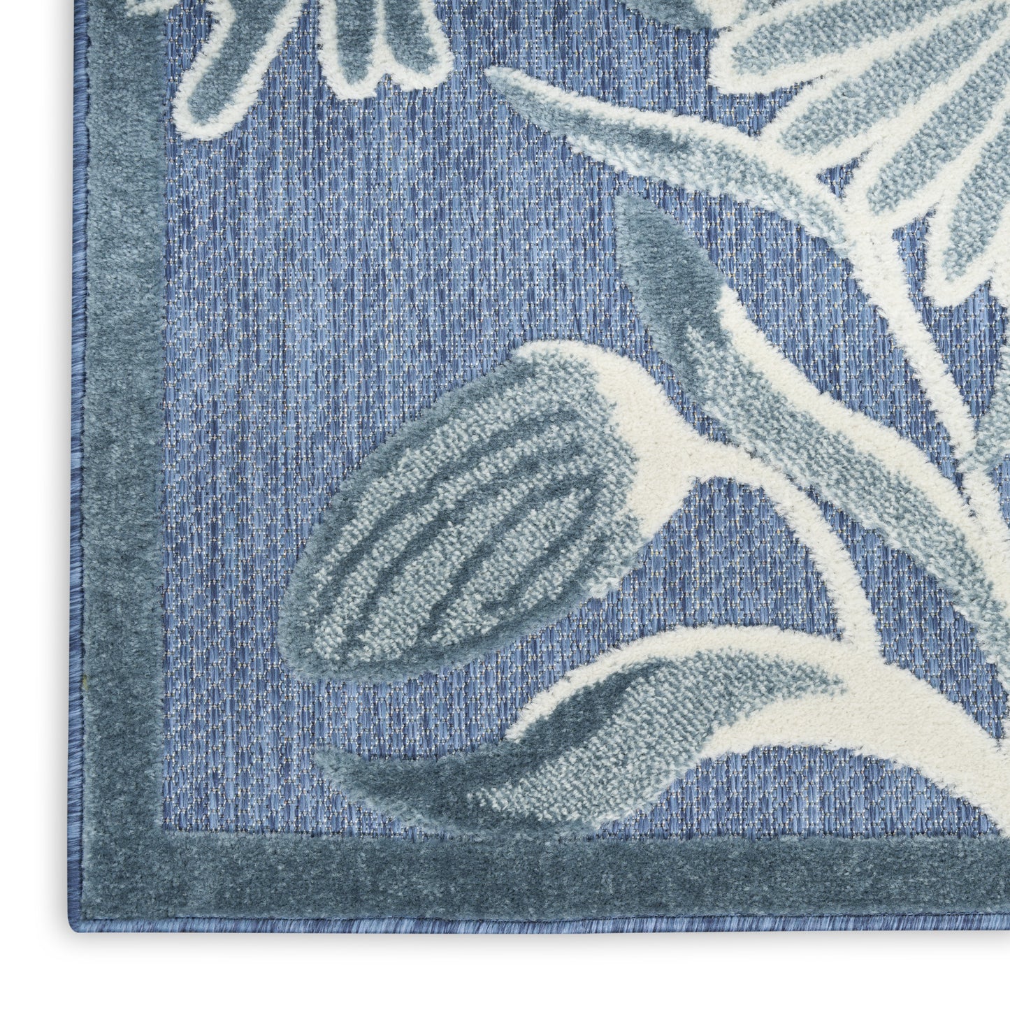 Blue area rug close-up with teal border; plush pile featuring cream-blue botanical leaves on woven blue background.