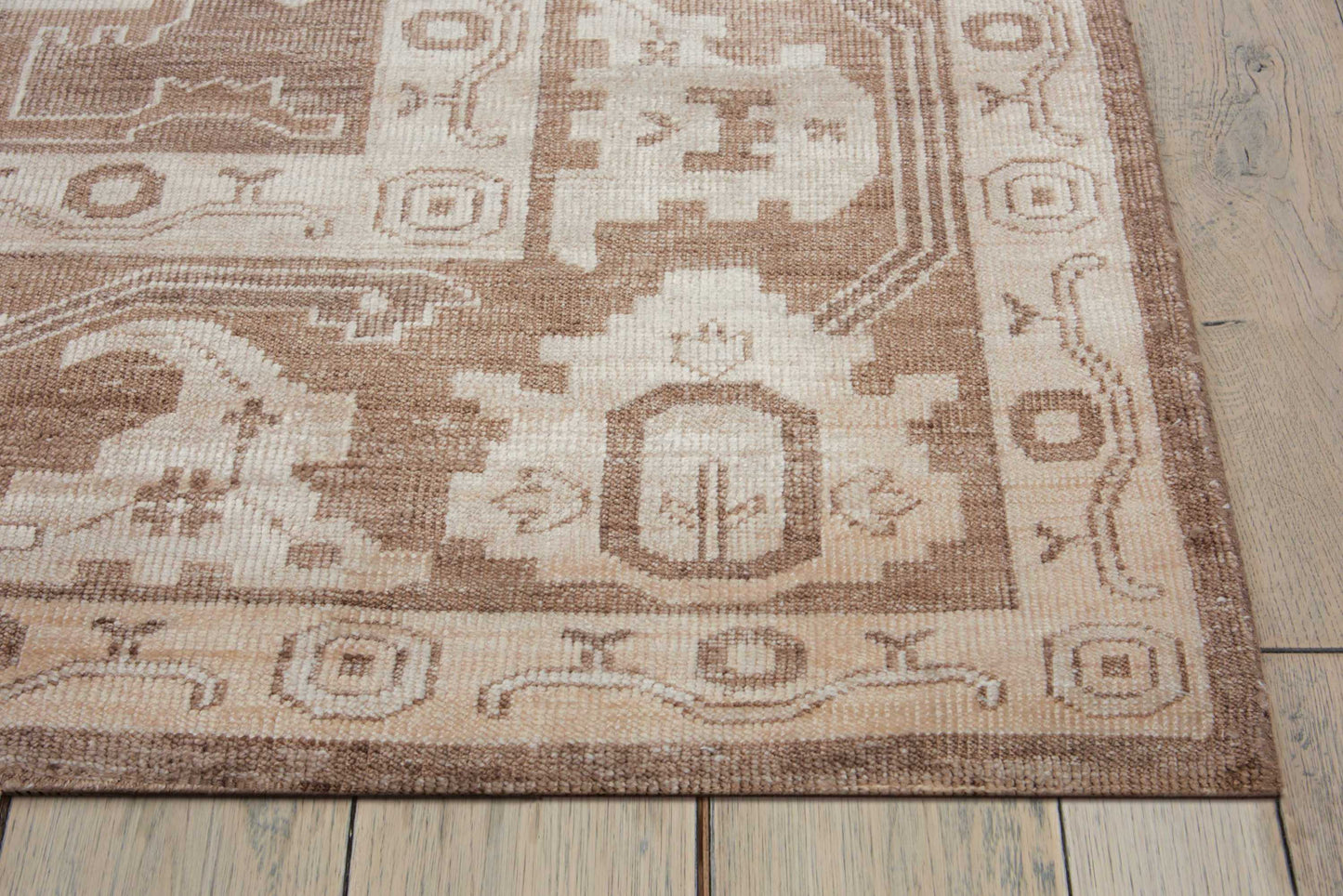 Rectangular brown and cream oriental rug with geometric border, laid on a wooden floor.