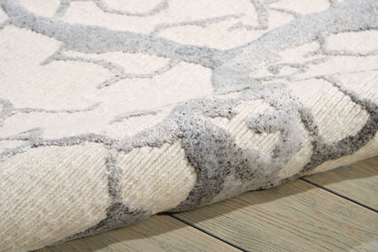 Beige and gray stone-mosaic patterned rug with soft plush pile, rolled edge on light wood floor.