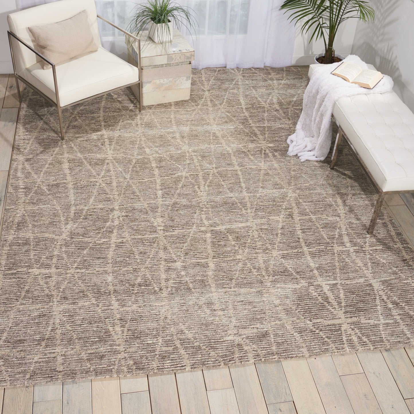 Beige woven rug with geometric criss-cross pattern on light wood floor; white cushioned chairs and a white tufted bench.