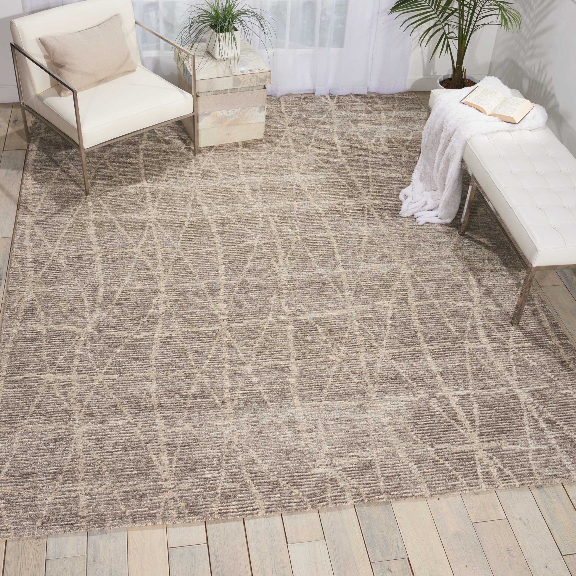 Beige woven rug with geometric criss-cross pattern on light wood floor; white cushioned chairs and a white tufted bench.