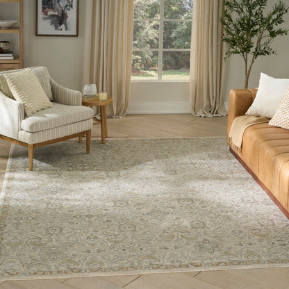 Muted gray-cream ornate area rug in a bright living room with beige curtains, cream chair, tan sofa and leafy plant.