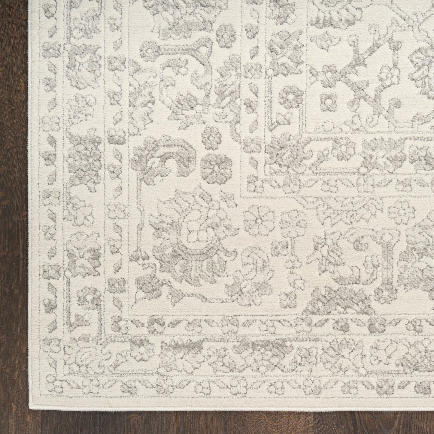 Cream rug with light grey Persian-style floral border and medallion pattern on dark wood floor.
