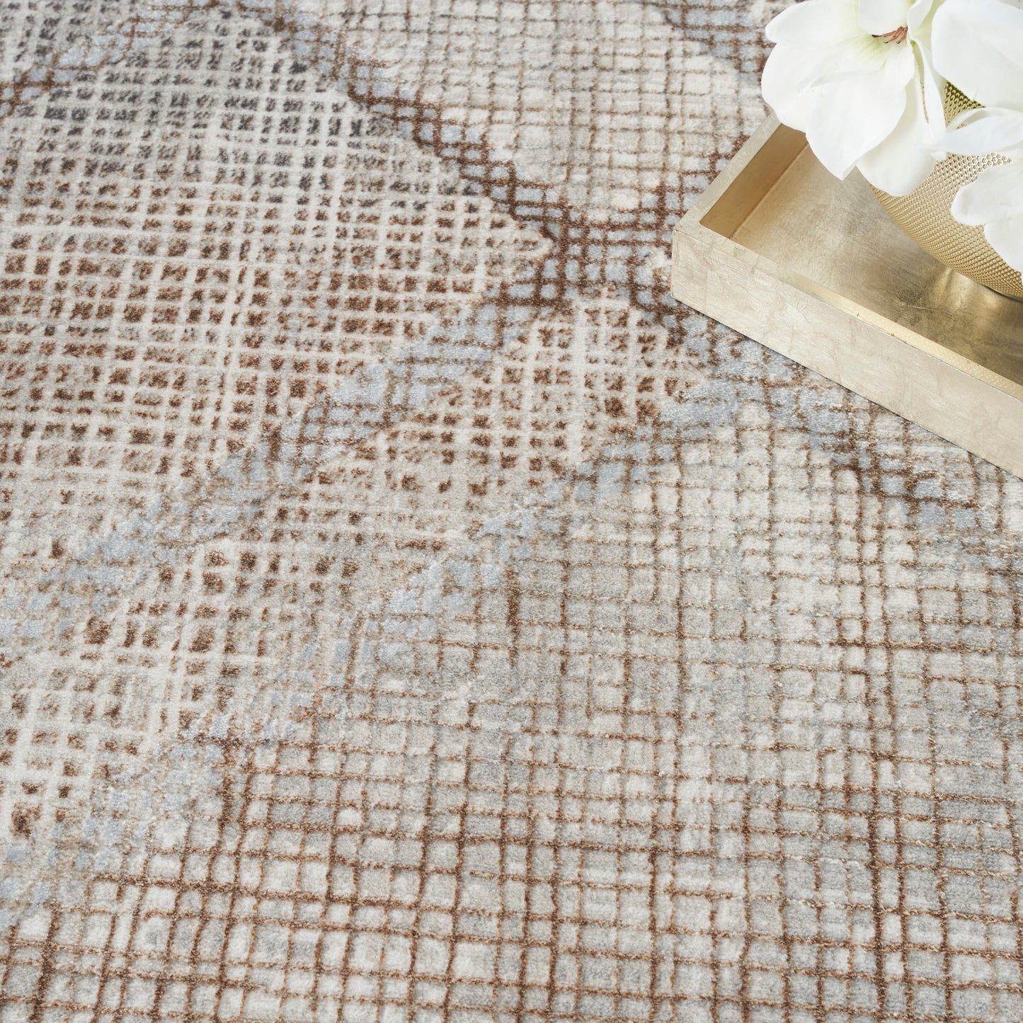 Beige abstract grid rug with brown lines and pale blue accents; gold tray with white flowers rests on edge.