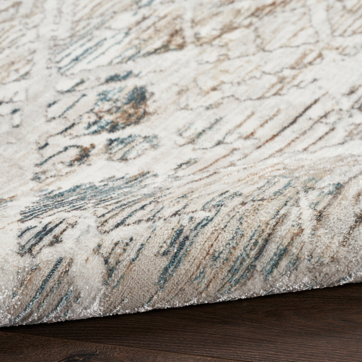 Beige cream area rug with blue-gray abstract strokes and soft textured pile, edge on dark wood floor.