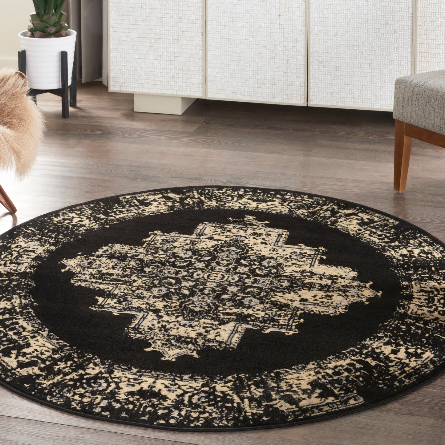 Round black oriental-style rug with beige distressed medallion pattern on dark wood floor.
