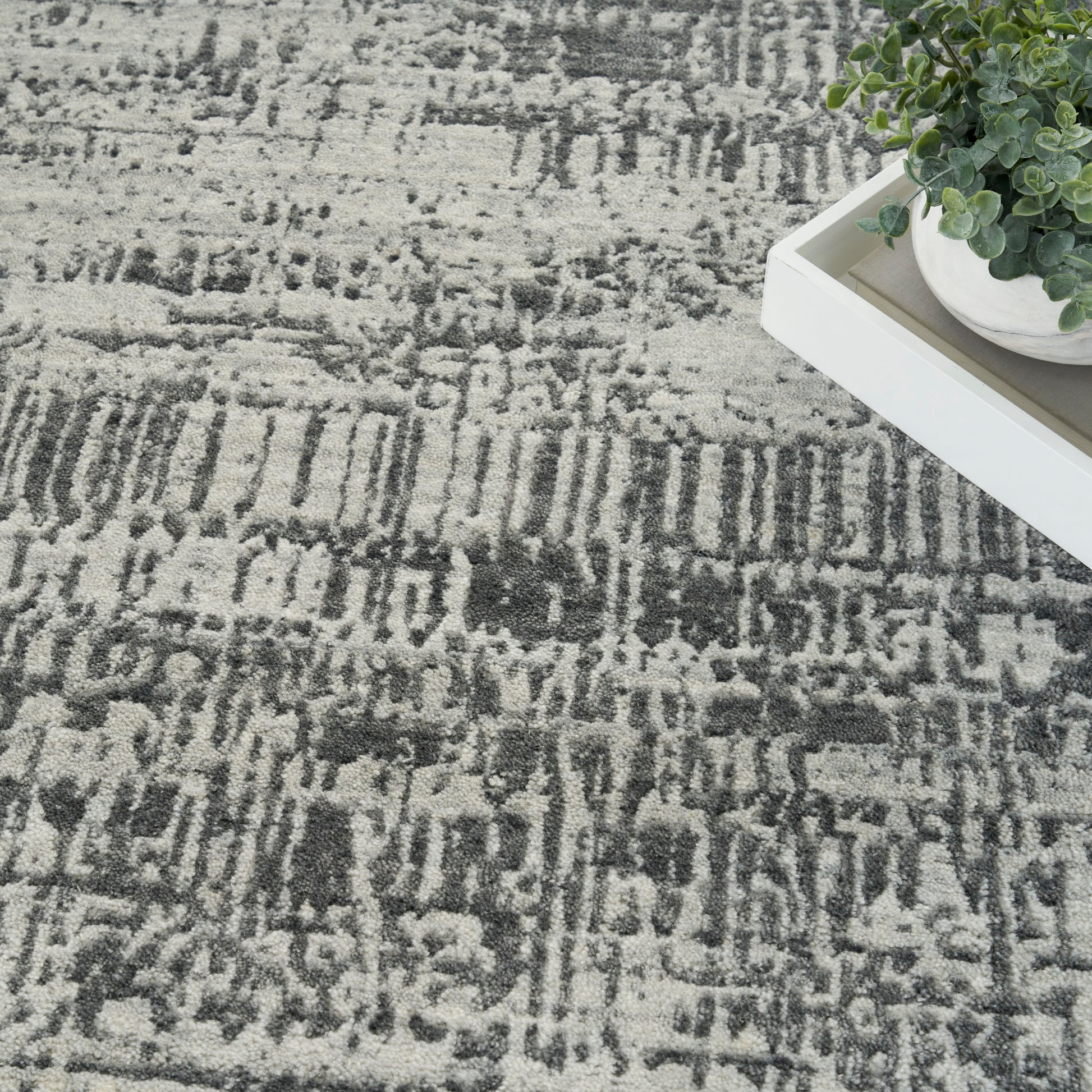 Modern gray and charcoal abstract patterned rug with a white tray and small potted plant.