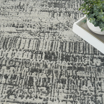 Modern gray and charcoal abstract patterned rug with a white tray and small potted plant.