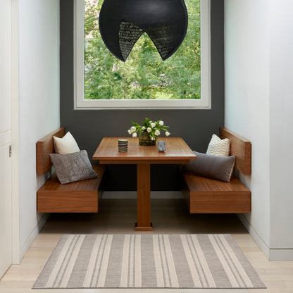 Cozy built-in wooden dining nook with rectangular table, gray walls, black pendant light, striped rug, and vase of flowers.