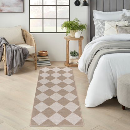 Beige and white diamond-pattern runner rug in a bright bedroom with a bed, wicker chair, and potted plants.