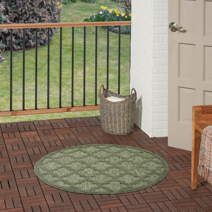 Round green braided outdoor rug on brick porch with wicker basket, white brick wall, wooden railing, and garden beyond.