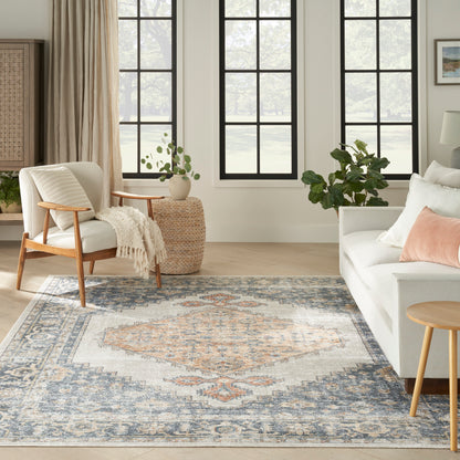 Neutral living room with large blue-gray oriental rug, cream sofa, wooden armchair, round wicker table, and greenery.