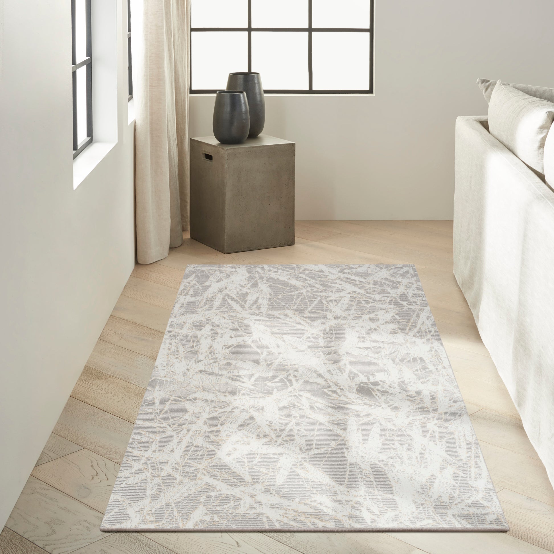 Rectangular abstract grey-and-white rug on light wood floor beside a concrete side table with black ceramic vases.