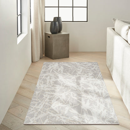 Rectangular abstract grey-and-white rug on light wood floor beside a concrete side table with black ceramic vases.