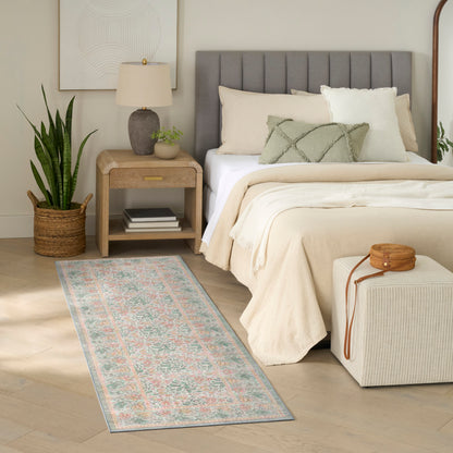 Neutral bedroom with gray upholstered headboard, cream bedding, pastel floral rug runner, snake plant in wicker basket, nightstand lamp.