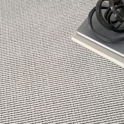Beige textured rug with a black coiled cord resting on top of stacked gray and white hardcover books.