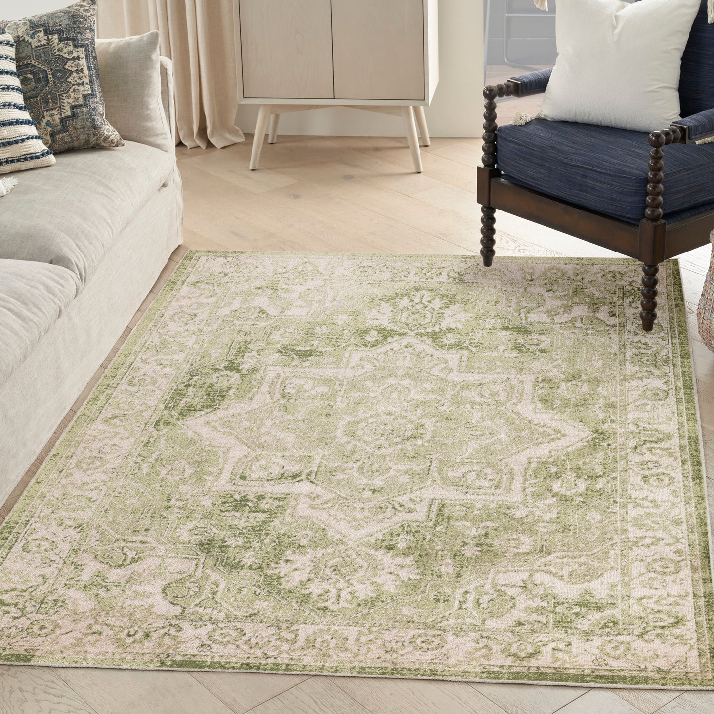 Green and cream oriental-style area rug in a light wood living room with a beige sofa and a navy armchair.