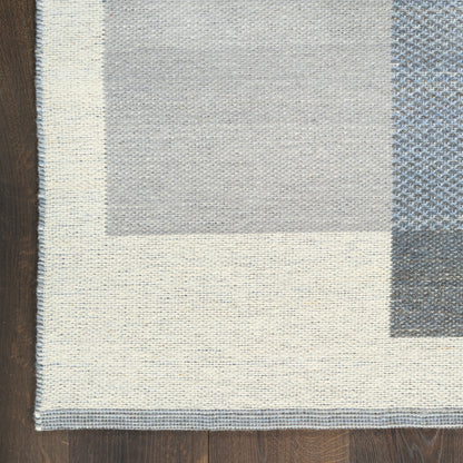 Neutral woven rug with cream border and light gray and blue-gray geometric blocks on dark wood floor.