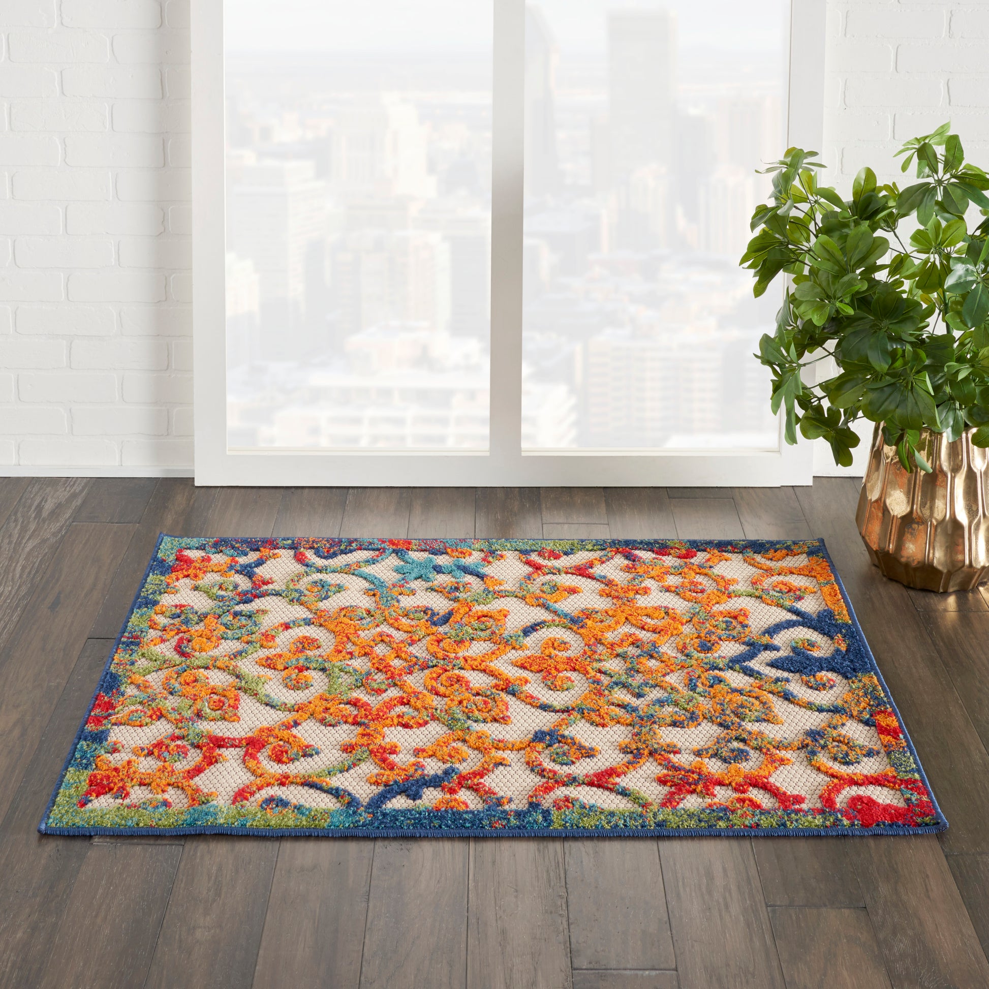 Colorful rectangular rug with orange, red, blue and teal swirls on dark wood floor beside a window and potted plant.