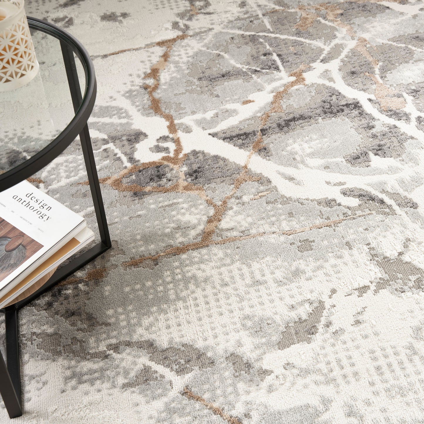 Neutral abstract rug in gray, white, beige & rust with a black round glass-topped coffee table & magazines.