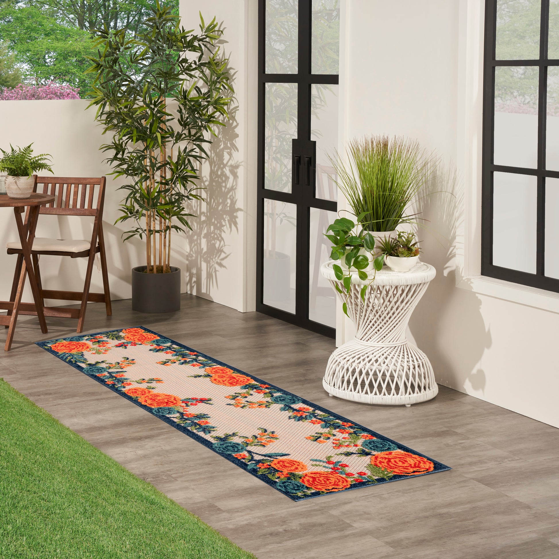 Floral runner rug with orange roses and blue border in a sunlit outdoor patio with potted plants.