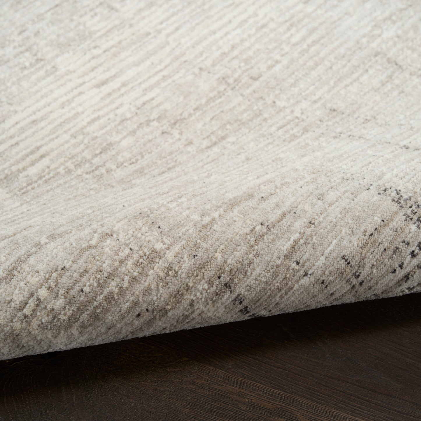 Cream beige area rug with soft pile, subtle speckled pattern, rolled edge on dark wood floor.