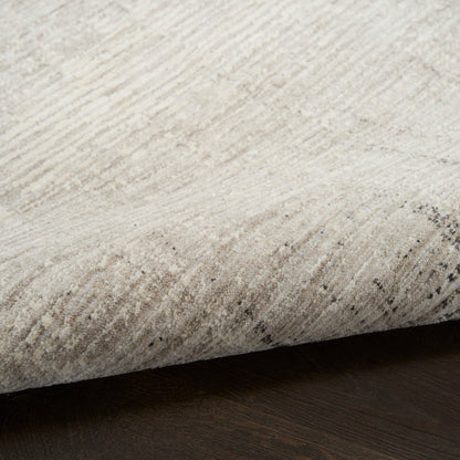 Cream beige area rug with soft pile, subtle speckled pattern, rolled edge on dark wood floor.
