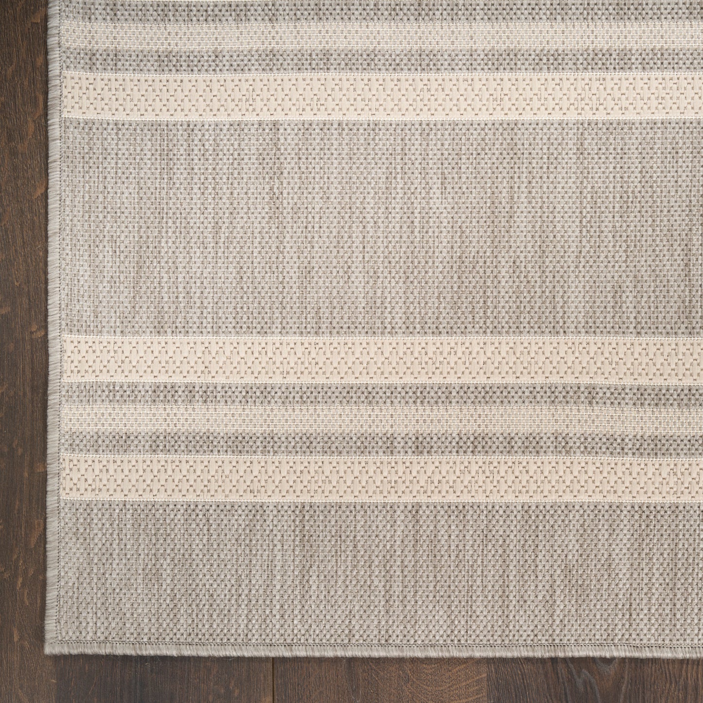 Flatwoven grey and cream striped rug with textured weave on dark wood floor, casual contemporary style.
