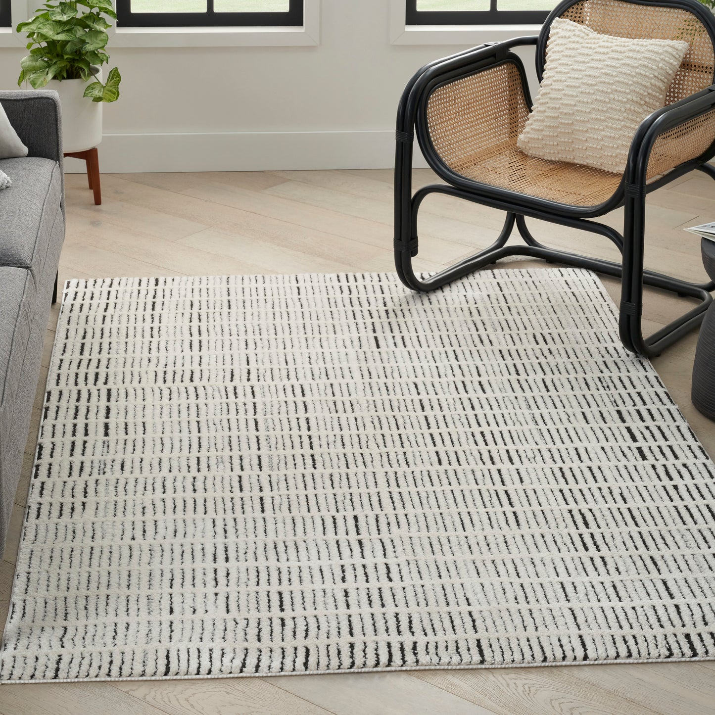 Rectangular cream rug with black linear grid in a bright living room beside a rattan chair and gray sofa.