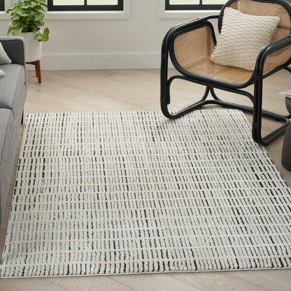 Rectangular cream rug with black linear grid in a bright living room beside a rattan chair and gray sofa.