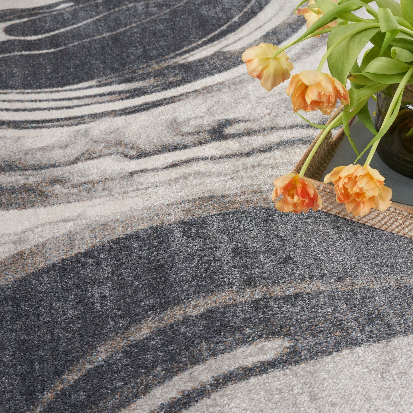 Abstract charcoal, gray and ivory rug with swirled pattern; plush texture beside orange tulips for decor.