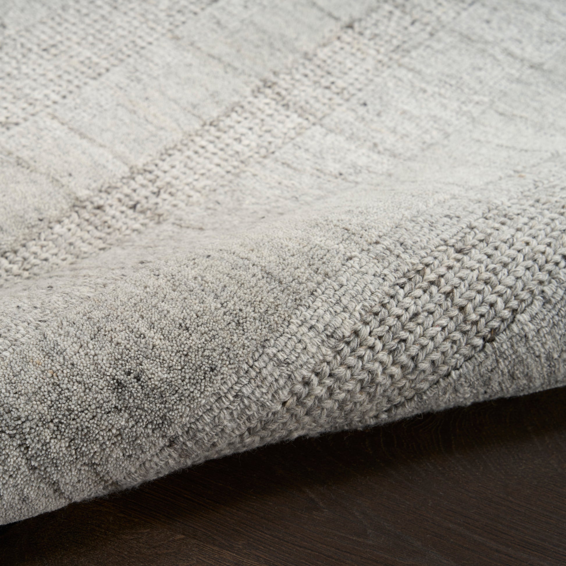 Light gray woven area rug with subtle checkered pattern, soft textured pile and folded edge.
