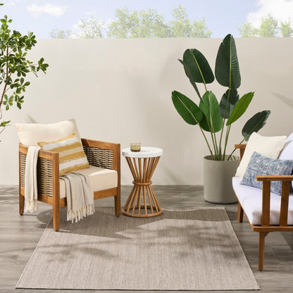 Outdoor seating with wooden frames, woven backs, beige cushions, striped pillow, throw, round white-top side table, plant.