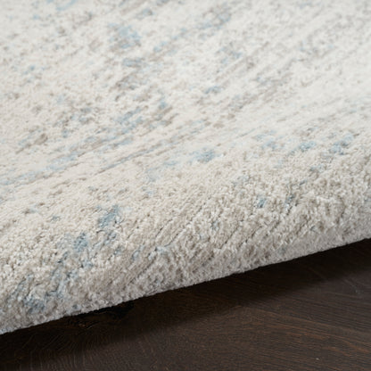 Close-up of soft, light gray rug with pale blue accents and plush cut-pile on dark wood floor.