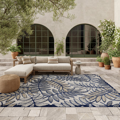 Outdoor patio with a beige sectional sofa on a blue leafy-pattern rug; terracotta pots and arched windows.