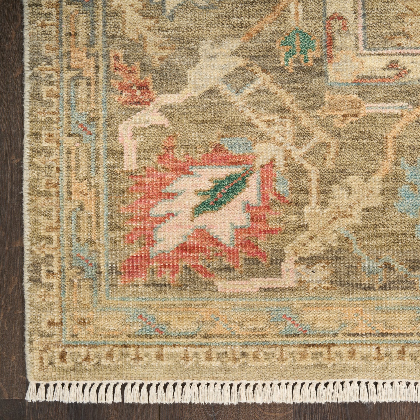 Woven wool oriental rug in beige tones with blue border, red leaf motif, geometric pattern, white fringe along bottom.