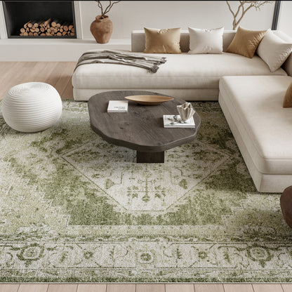 Vintage 9' x 12' green rug in a living room with a beige sectional, neutral cushions, a round white knitted pouf, and a dark live-edge wood coffee table.