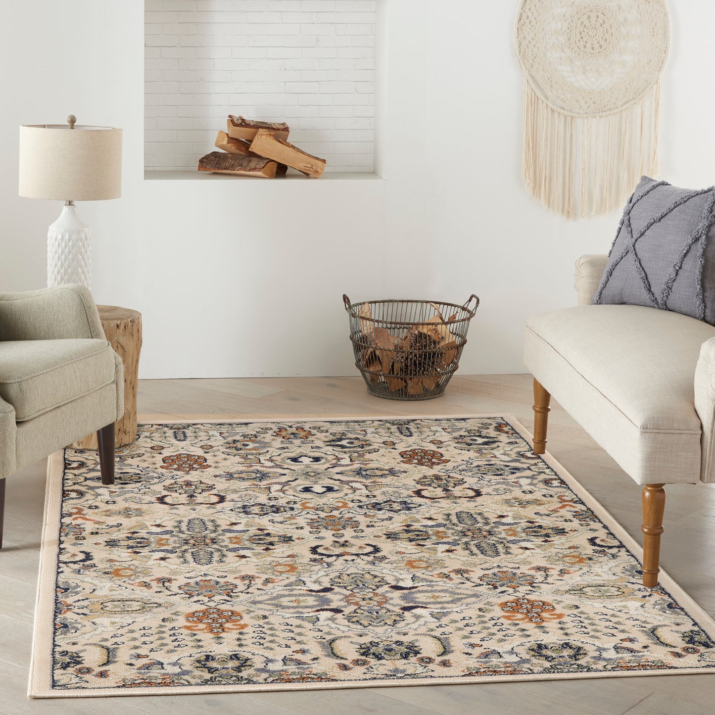 Neutral living room with beige seating, blue patterned area rug, log basket, fireplace alcove, & woven wall hanging.
