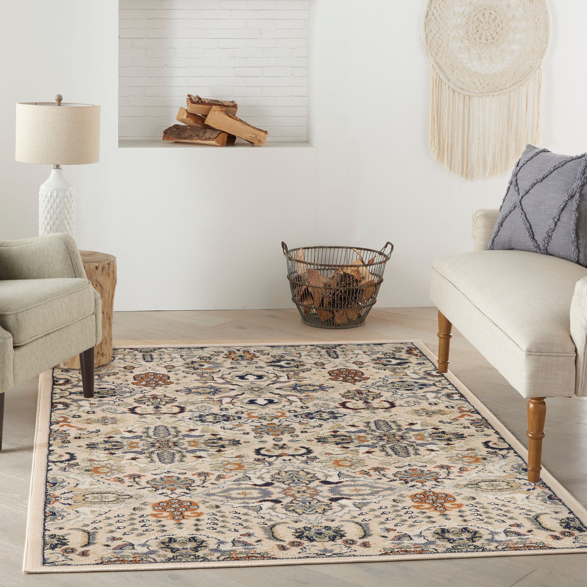 Neutral living room with beige seating, blue patterned area rug, log basket, fireplace alcove, & woven wall hanging.