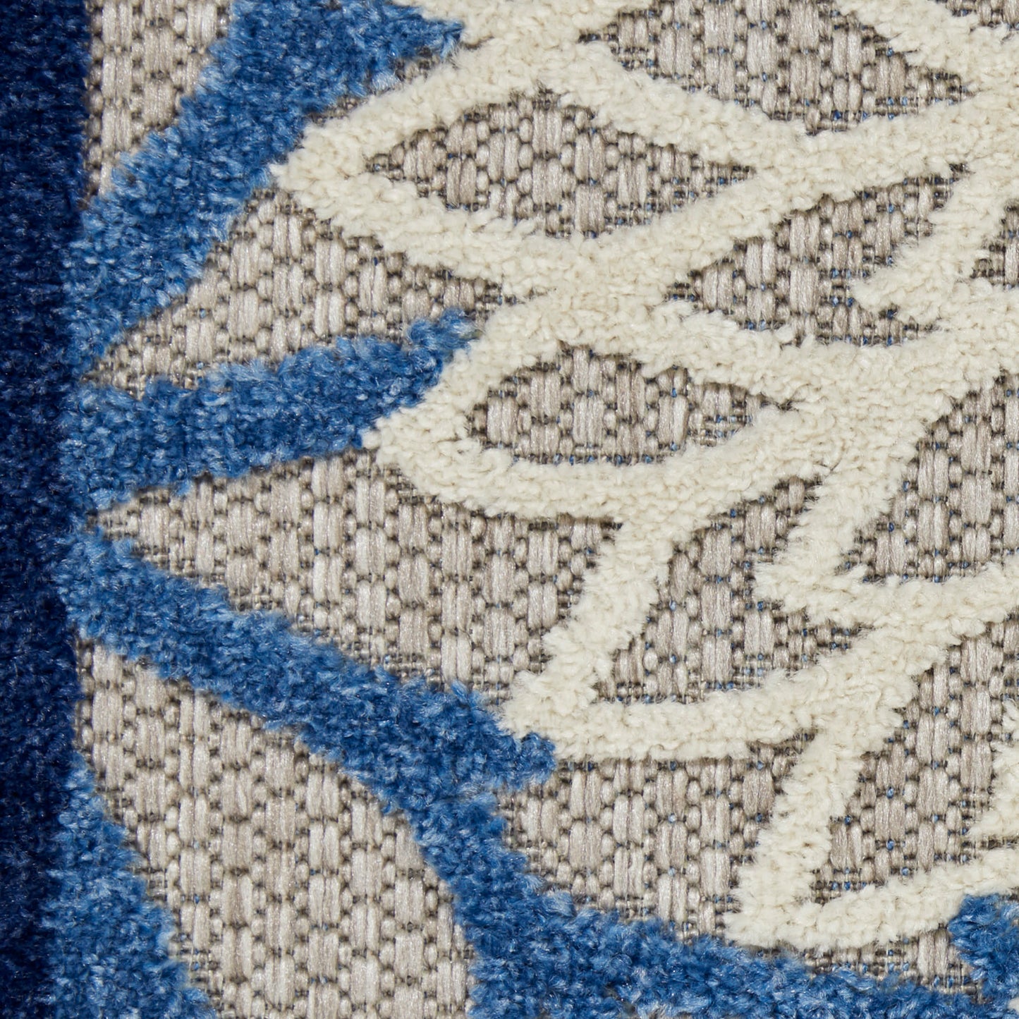 Close-up of a beige woven rug with white geometric lattice pattern and blue shaggy pile accents.