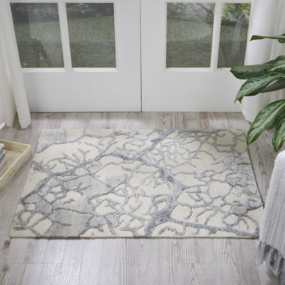 Rectangular cream area rug with grey abstract branch pattern on light wood floor by glass-paneled double doors.